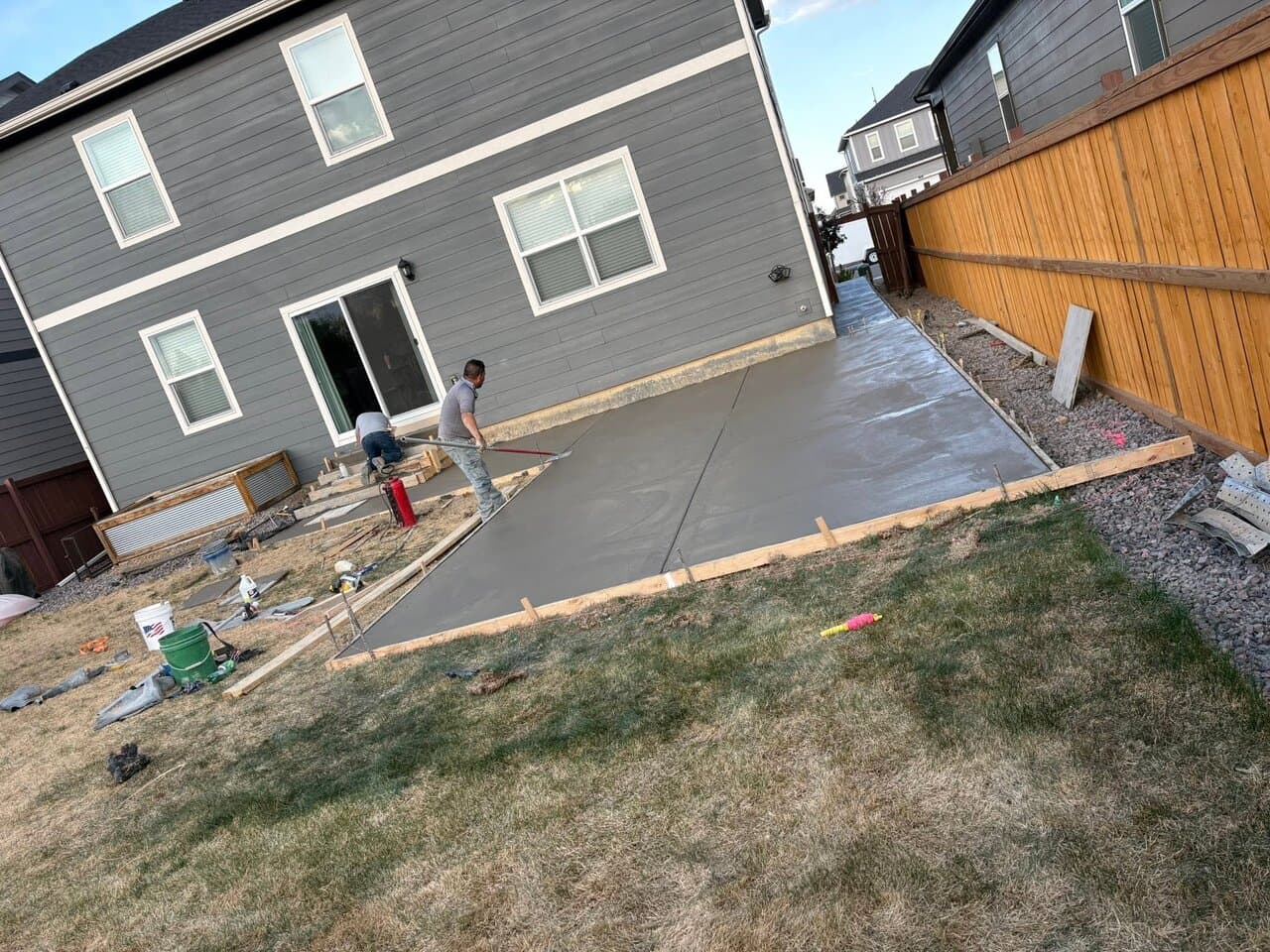 Workers pouring and finishing concrete for a patio next to a house