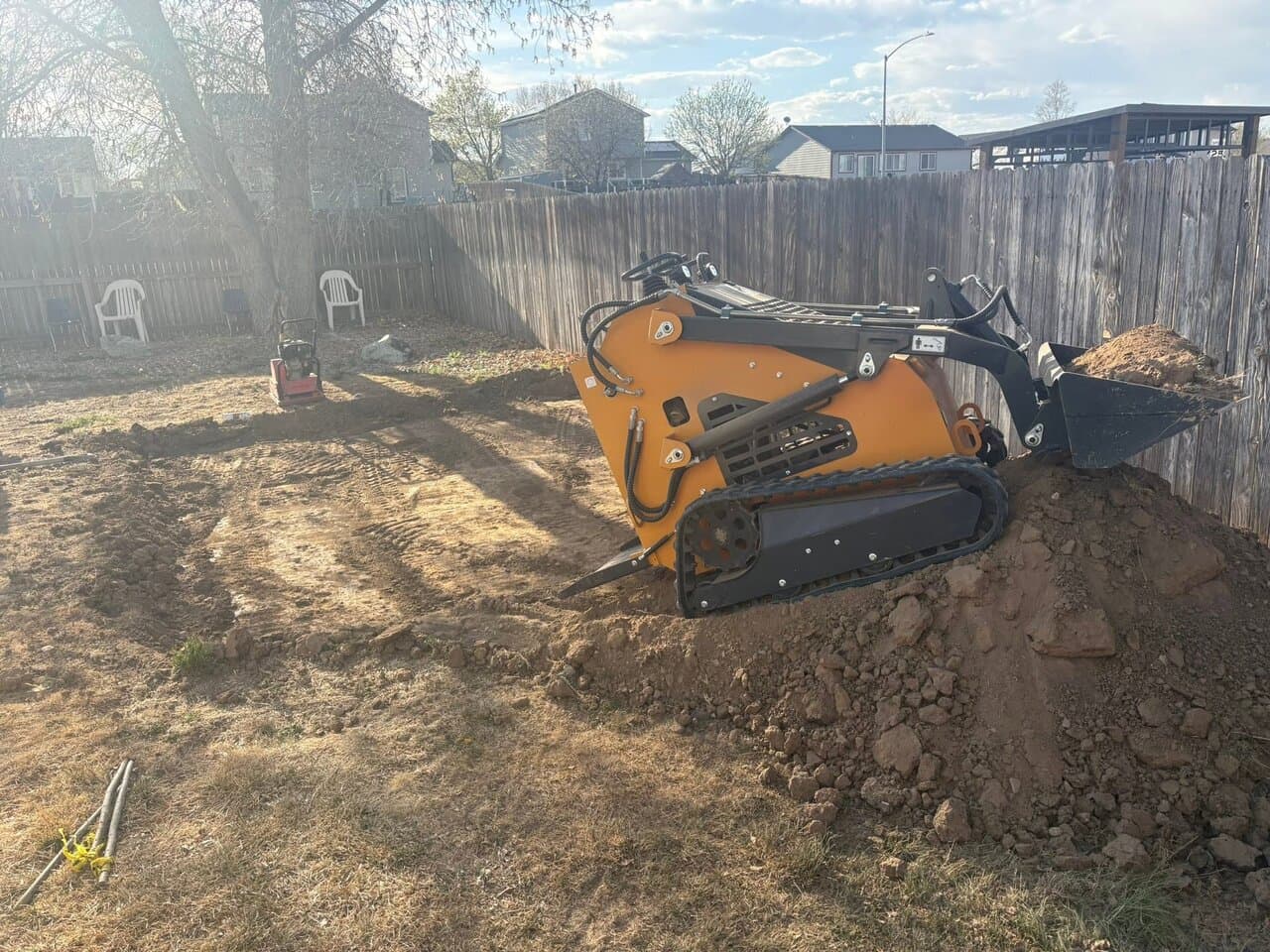 Compact track loader on a dirt pile in a residential backyard