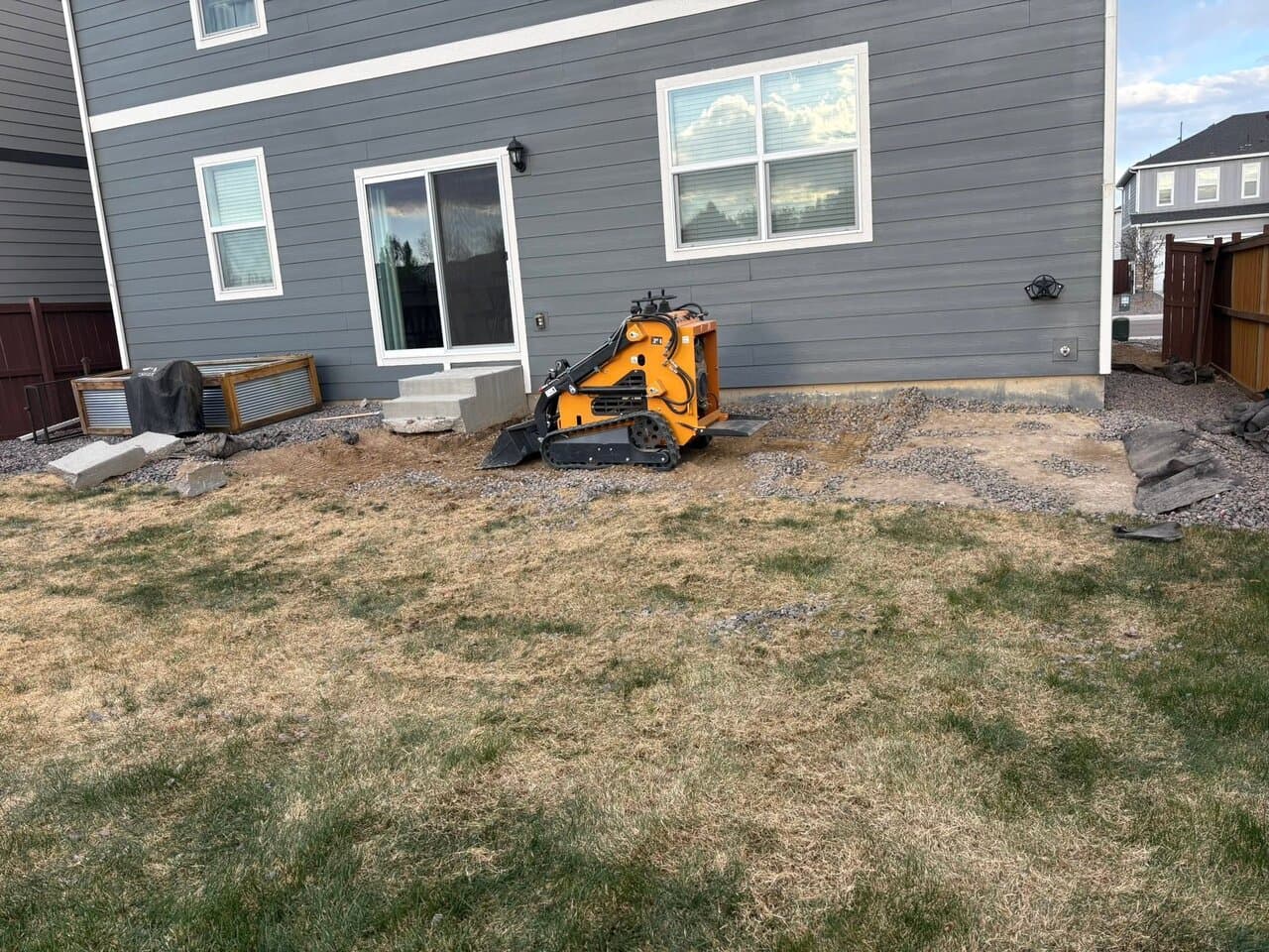 Yellow skid-steer loader next to a house during site preparation